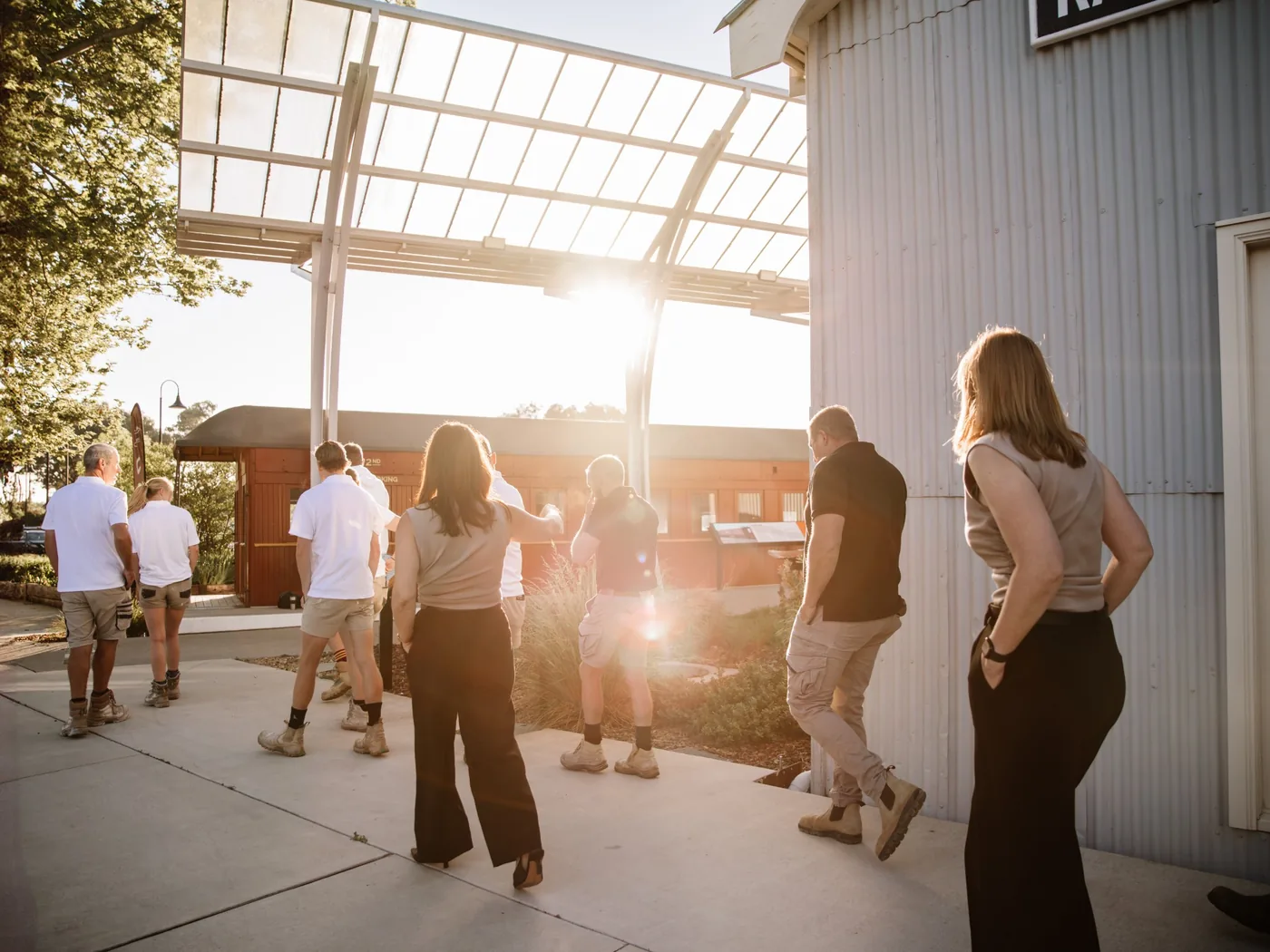 A group of people in work clothes walking together in golden afternoon light at a railway station